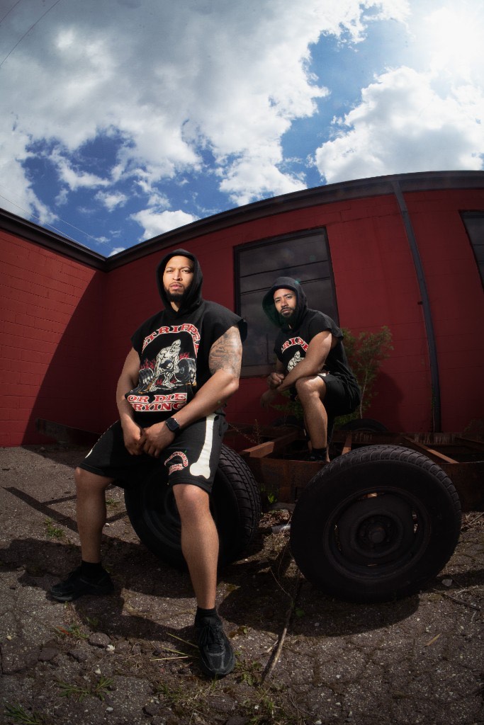 Two athletes in GRODT cut-off hoodies resting on trailer tires
